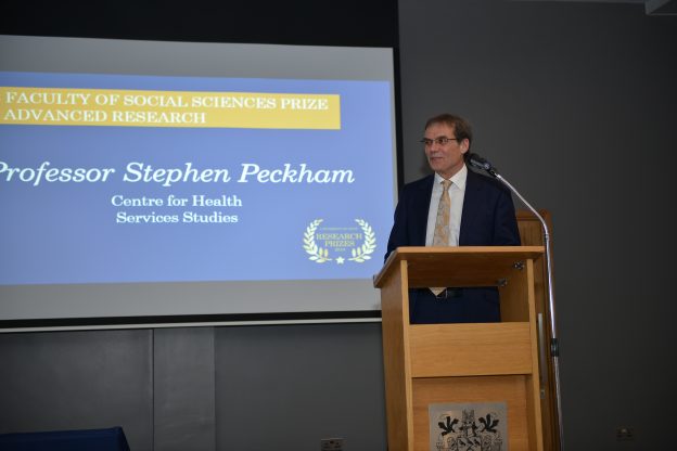 Professor Stephen Peckham standing on a podium on stage giving a talk with a projector screen behind him saying: Faculty of Social Sciences Prize and Advanced Research Professor Stephen Peckham Centre for Health Services Studies