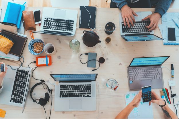 People working on five laptops together on a desk.